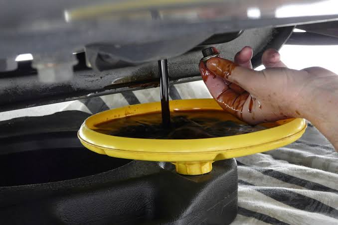 Used engine oil draining from a sump plug into a collection pan