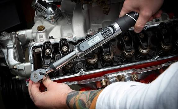 Hands using a digital torque wrench on a cylinder head fastener