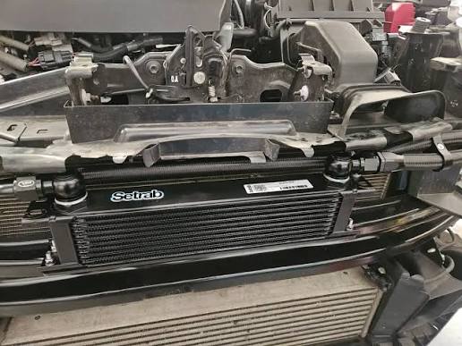 Auxiliary oil cooler core mounted behind the front structure of a car